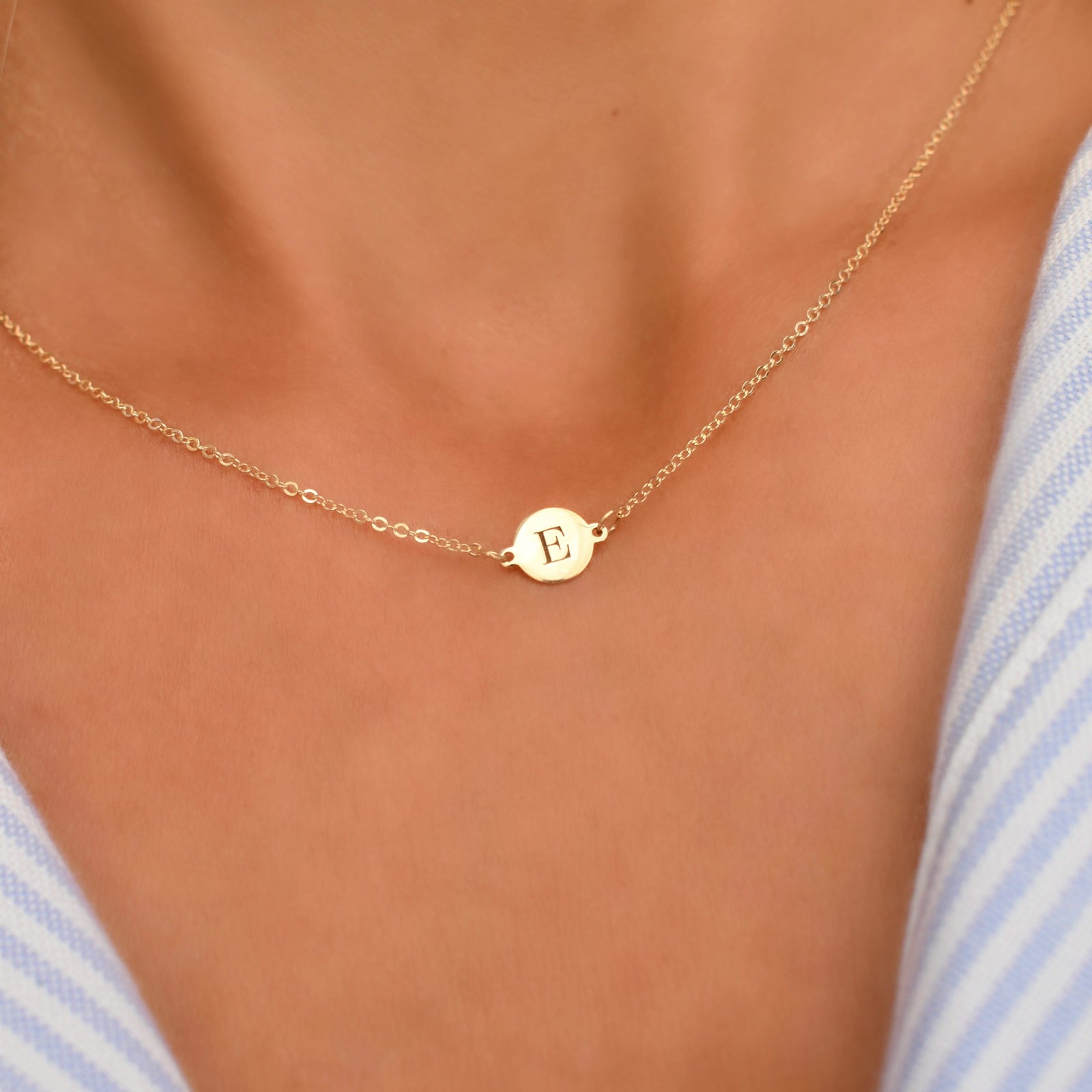 Woman with a 14k yellow gold cable chain necklace featuring one 1/4” flat disc engraved with the letter E