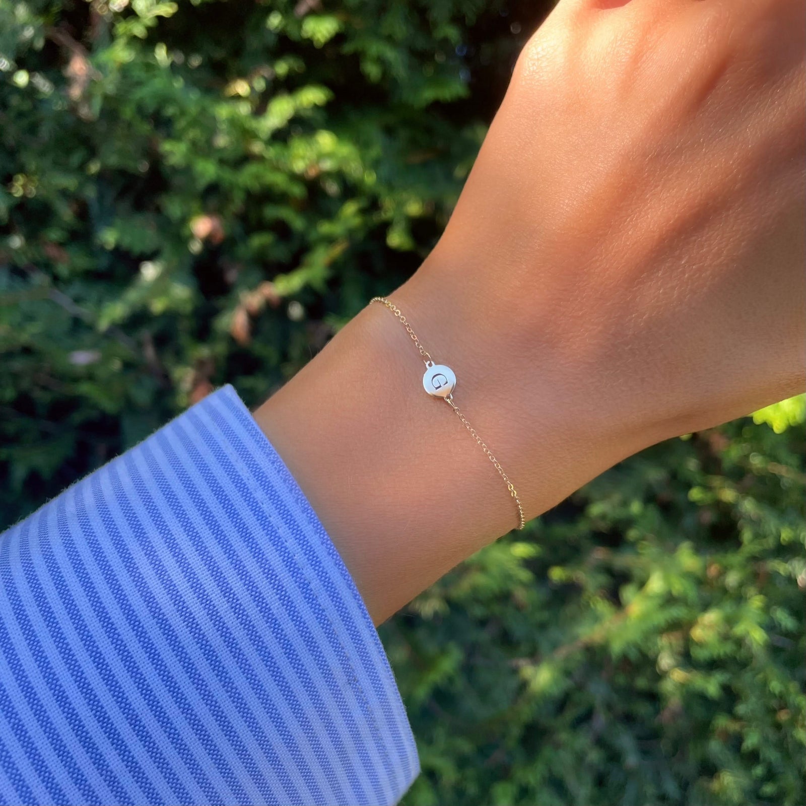 Woman wearing a 14k yellow gold cable chain bracelet featuring one 1/4” flat disc engraved with the letter G