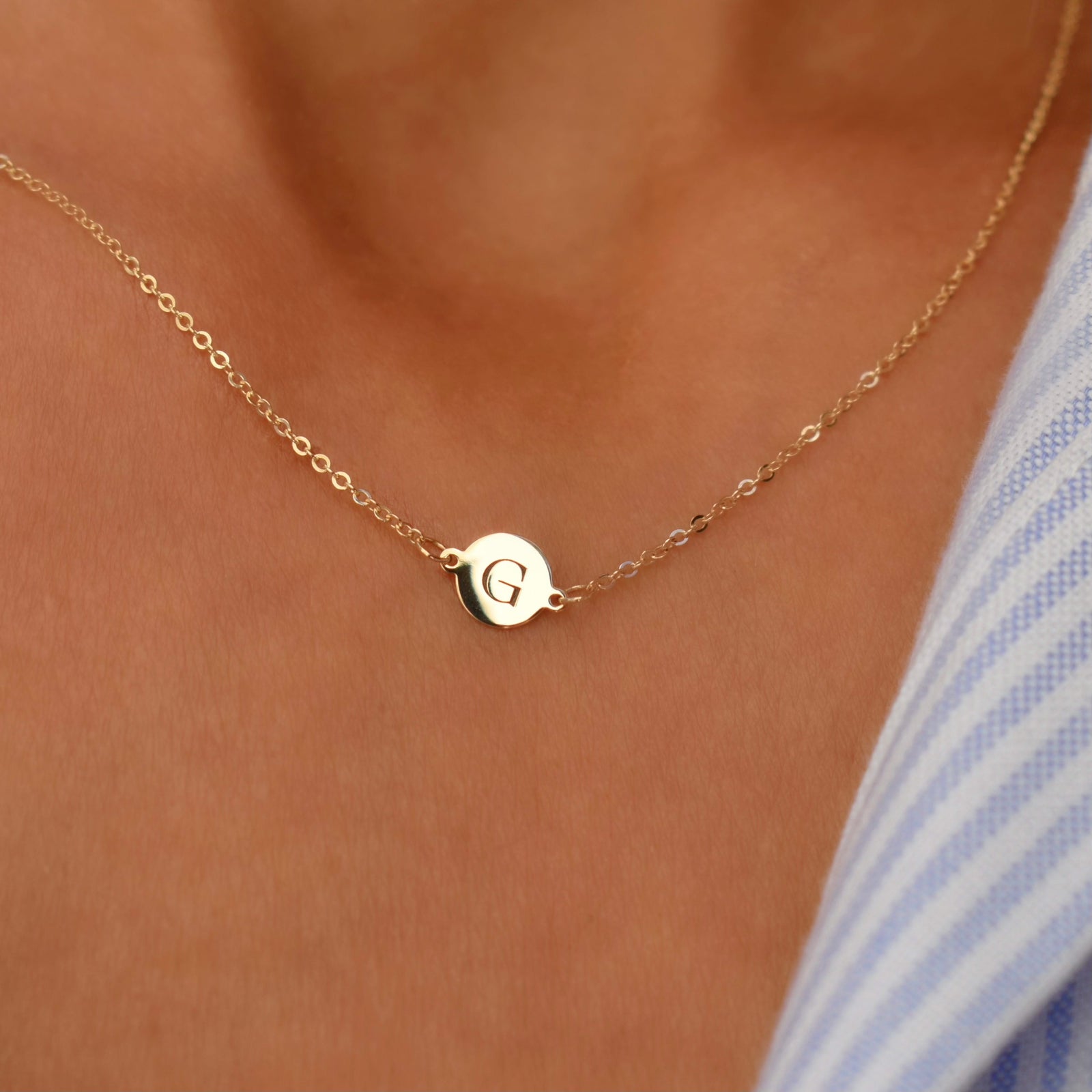 Woman wearing a 14k yellow gold cable chain necklace featuring one 1/4” flat disc engraved with the letter G