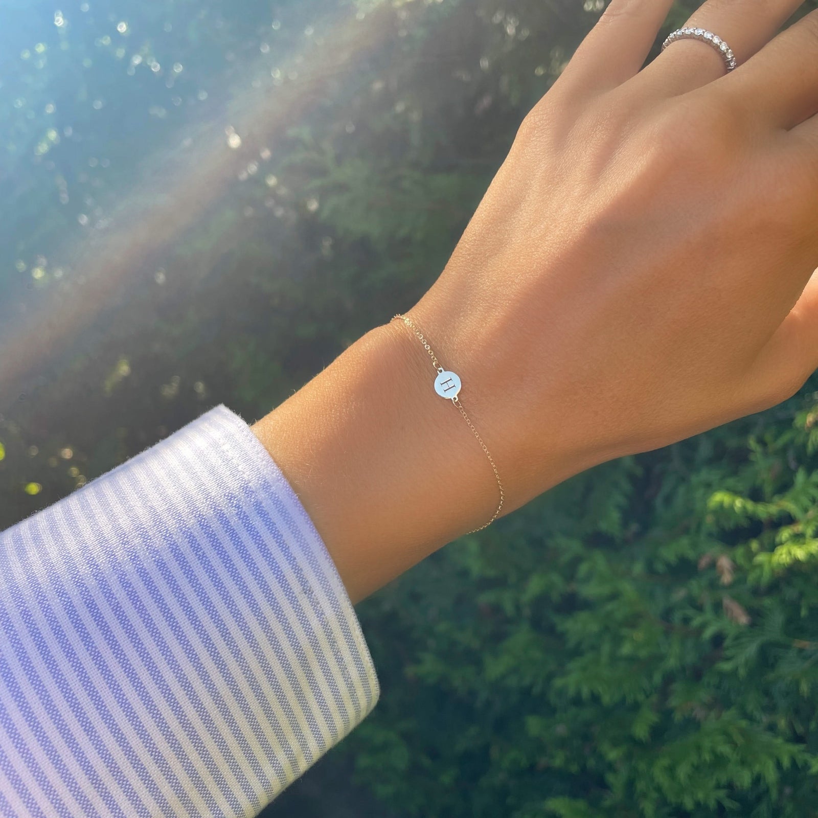 Woman wearing a 14k yellow gold cable chain bracelet featuring one 1/4” flat disc engraved with the letter H