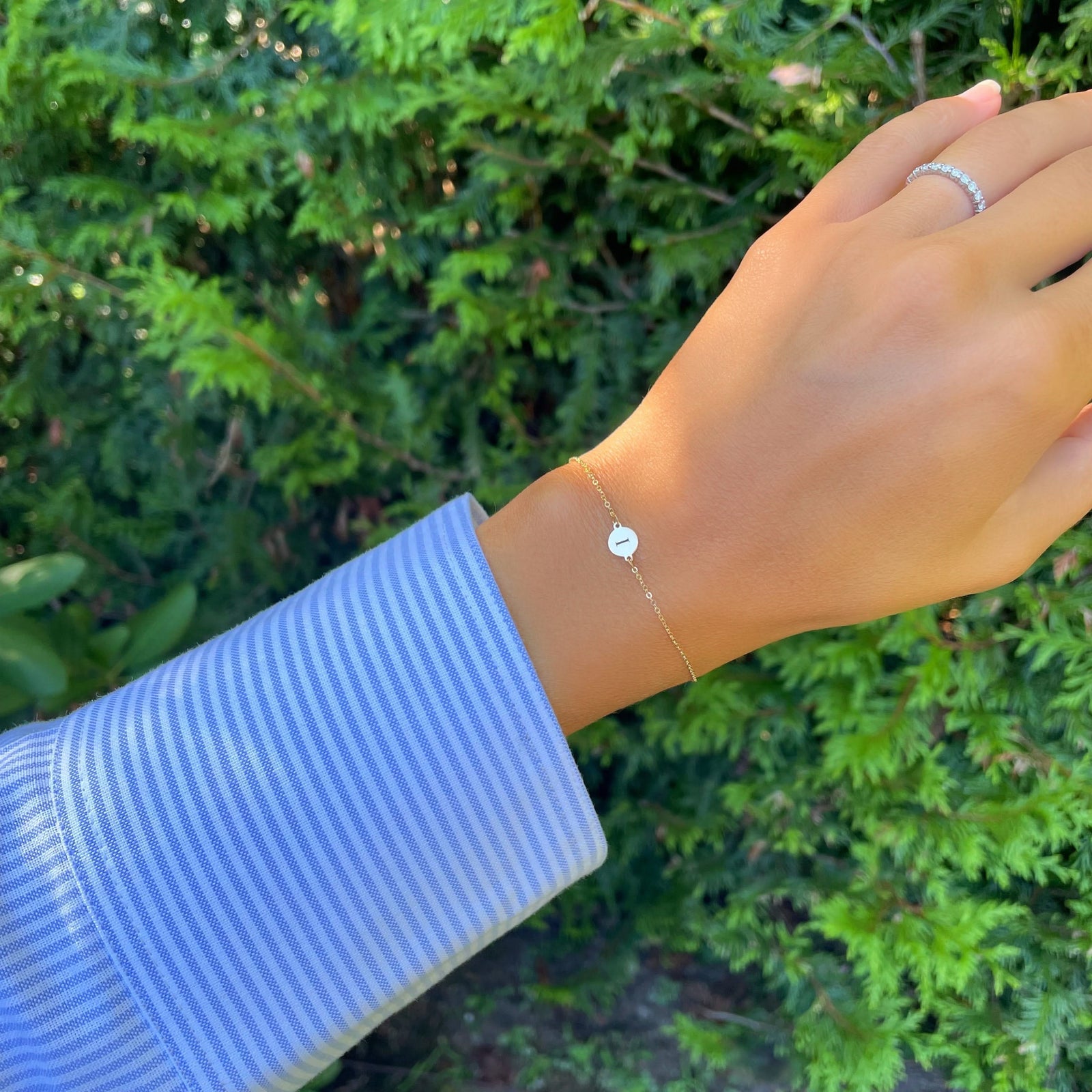 Hand wearing a 14k yellow gold cable chain bracelet featuring one 1/4” flat disc engraved with the letter I