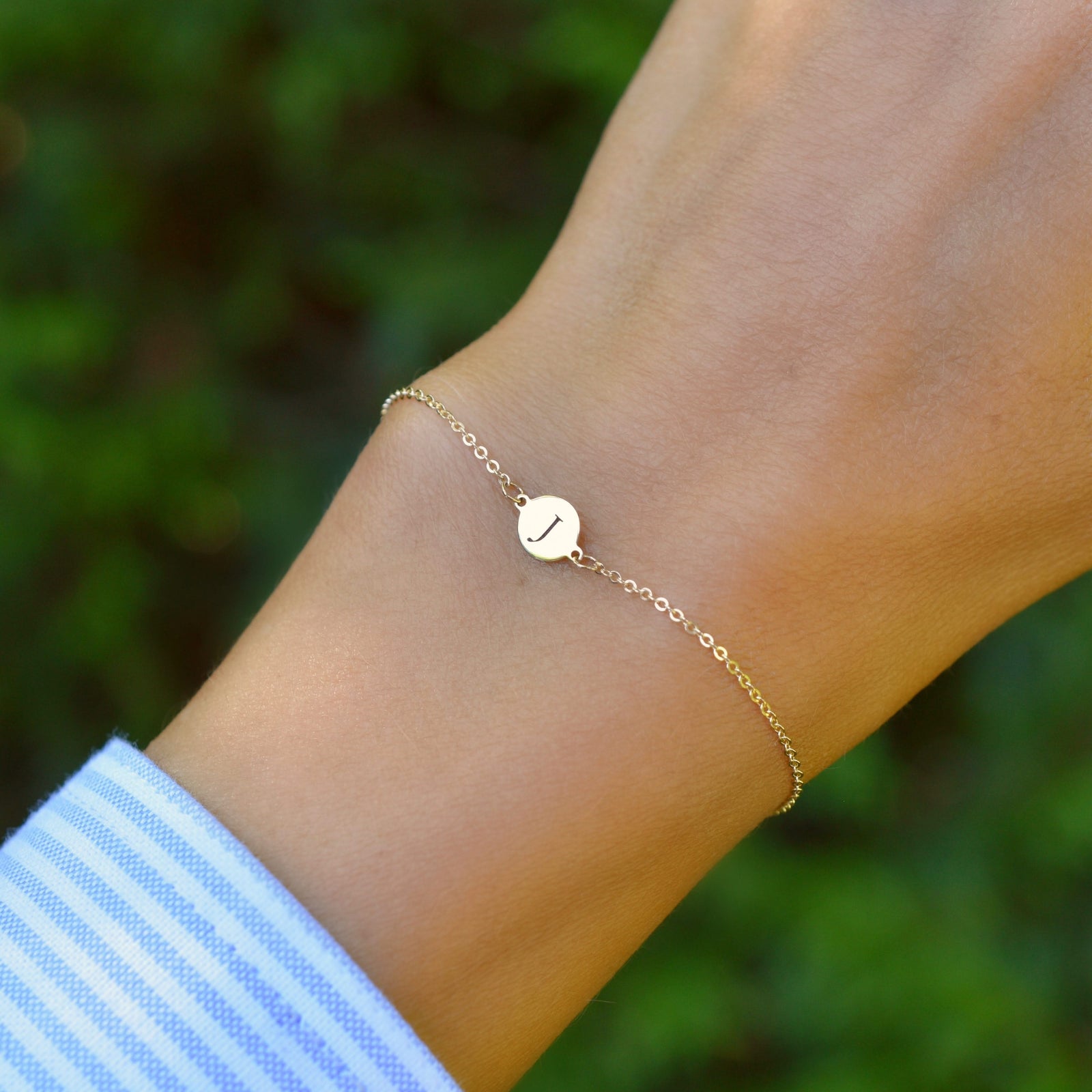 Woman wearing a 14k yellow gold cable chain bracelet featuring one 1/4” flat disc engraved with the letter J