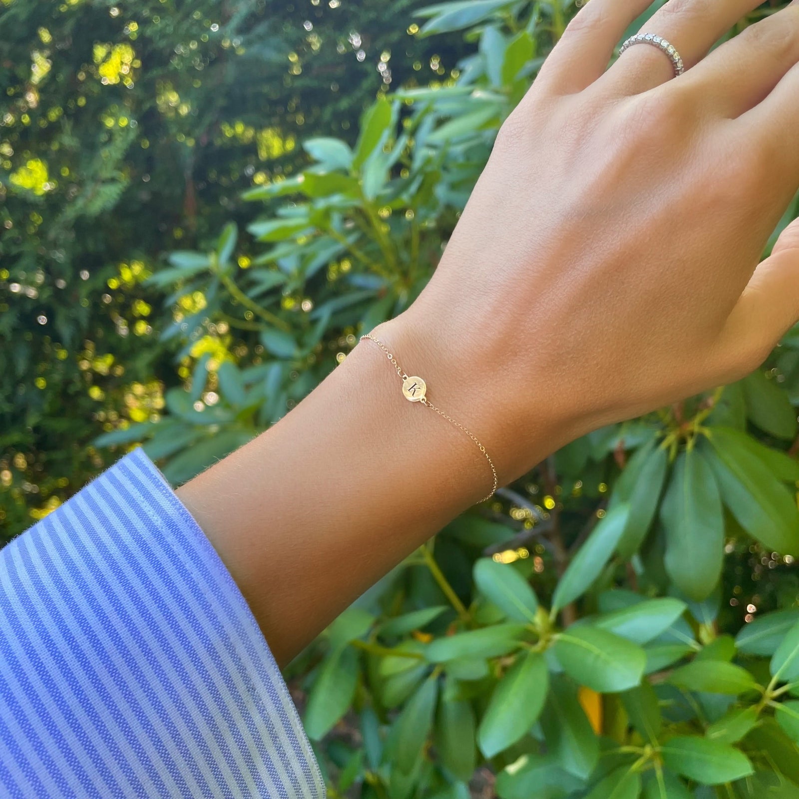 Woman wearing a 14k yellow gold cable chain bracelet featuring one 1/4” flat disc engraved with the letter K