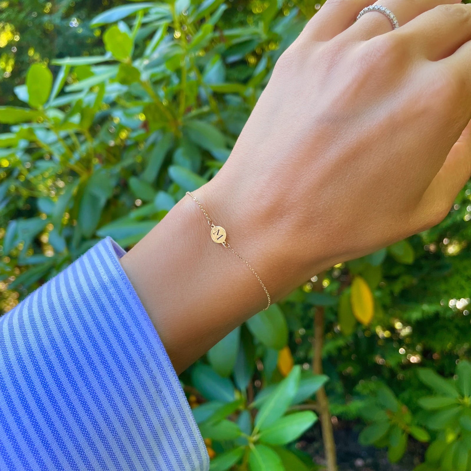 Woman wearing a 14k yellow gold cable chain bracelet featuring one 1/4” flat disc engraved with the letter M