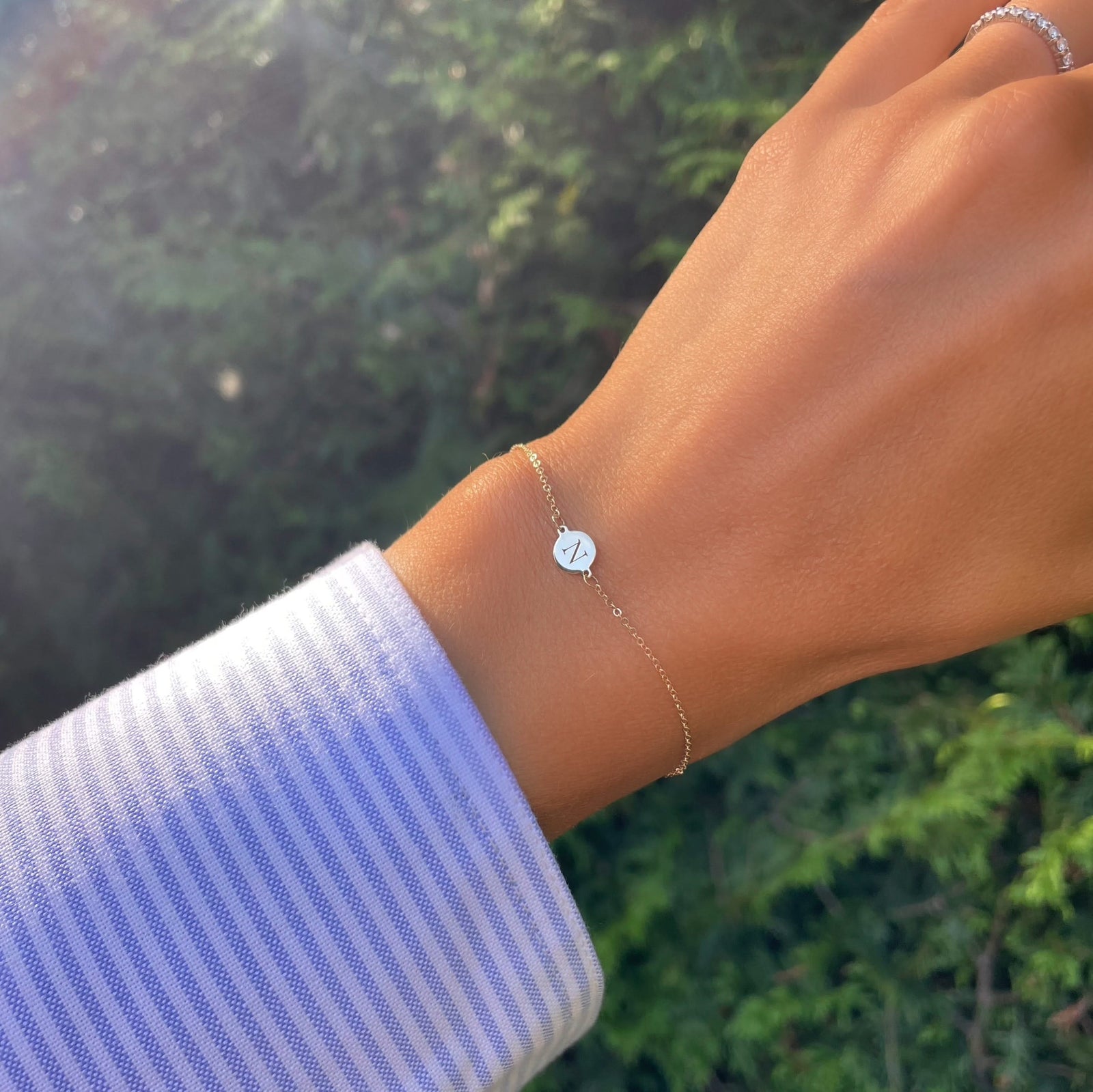 Woman wearing a 14k yellow gold cable chain bracelet featuring one 1/4” flat disc engraved with the letter N