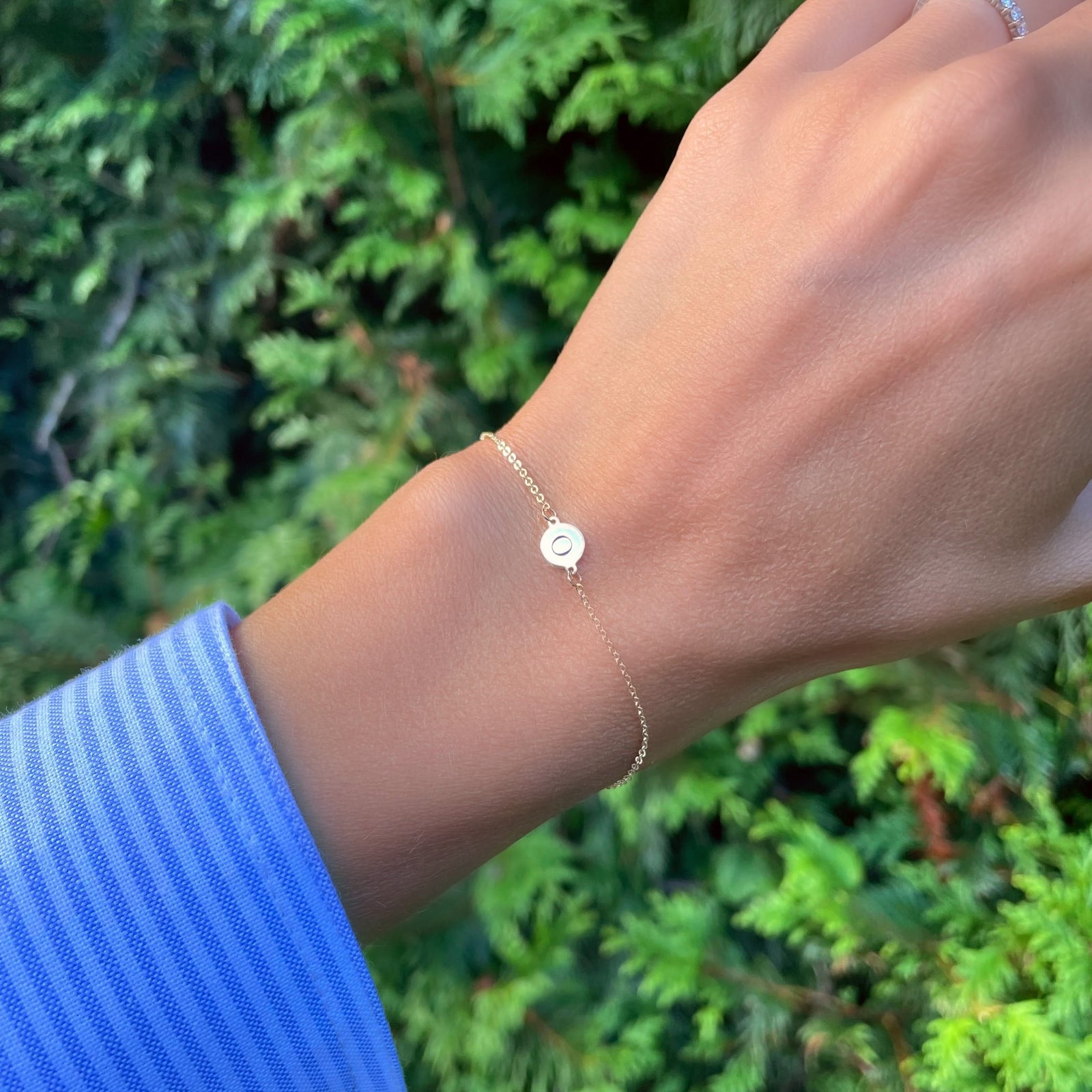 Woman wearing a 14k yellow gold cable chain bracelet featuring one 1/4” flat disc engraved with the letter O