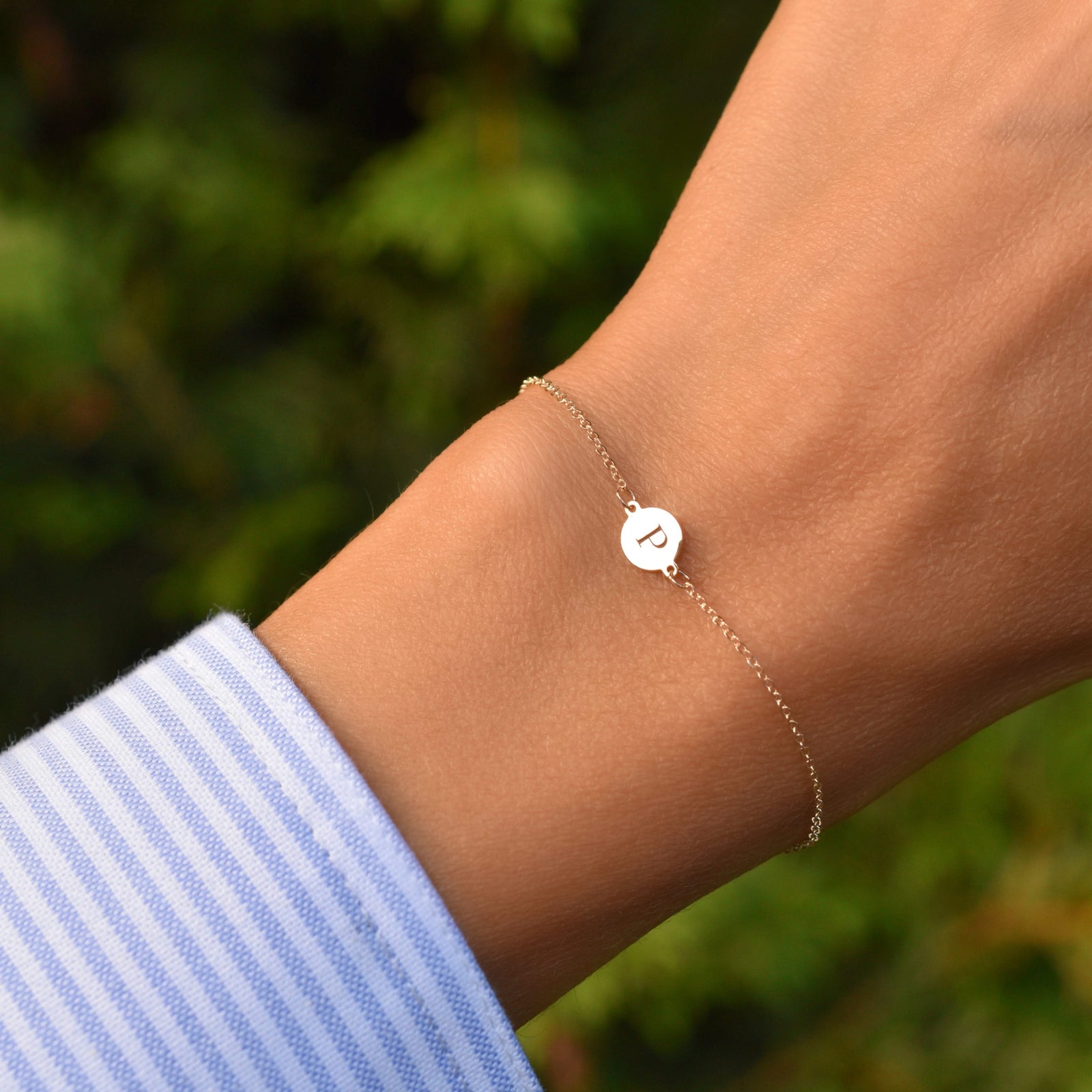Woman wearing a 14k yellow gold cable chain bracelet featuring one 1/4” flat disc engraved with the letter P