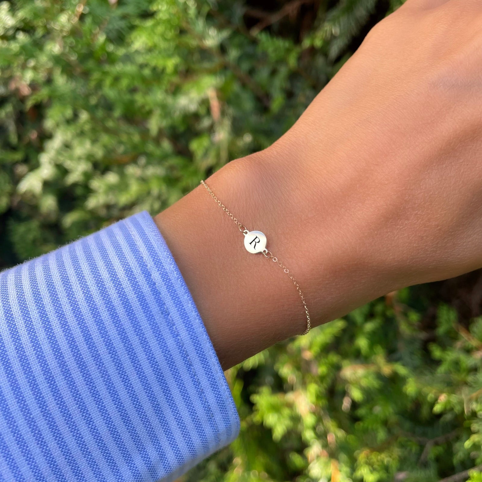 Woman wearing a 14k yellow gold cable chain bracelet featuring one 1/4” flat disc engraved with the letter R