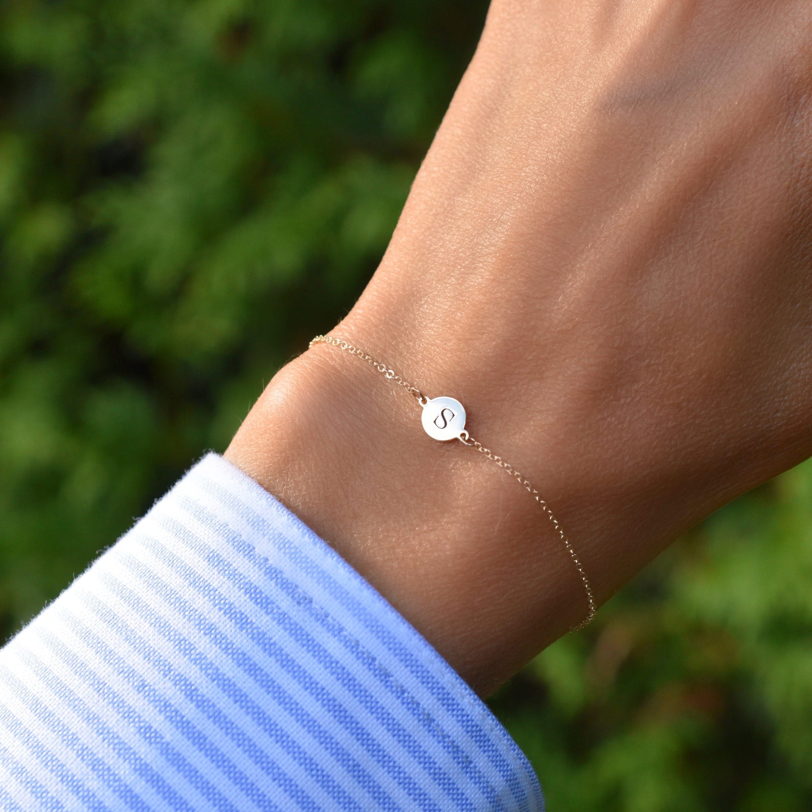 Woman wearing a 14k yellow gold cable chain bracelet featuring one 1/4” flat disc engraved with the letter S