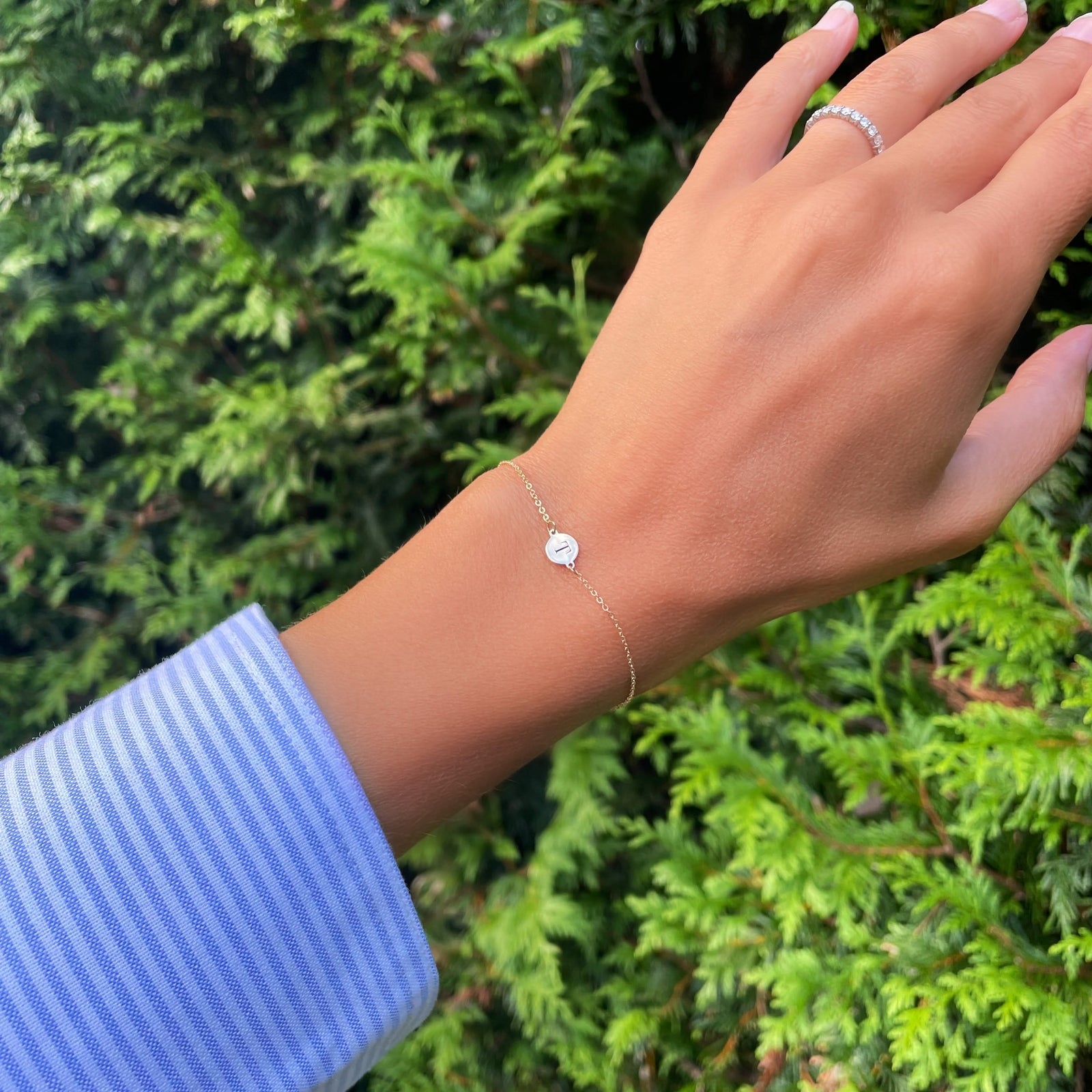 Woman wearing a 14k yellow gold cable chain bracelet featuring one 1/4” flat disc engraved with the letter T