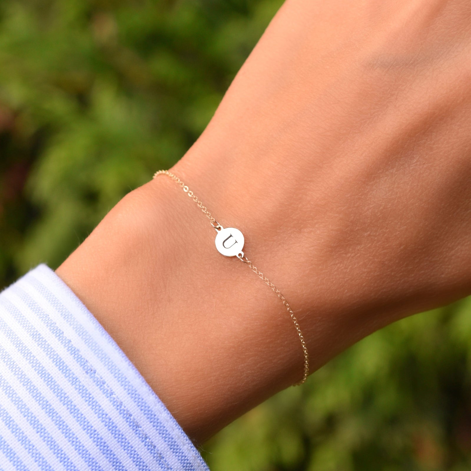 Woman wearing a 14k yellow gold cable chain bracelet featuring one 1/4” flat disc engraved with the letter U