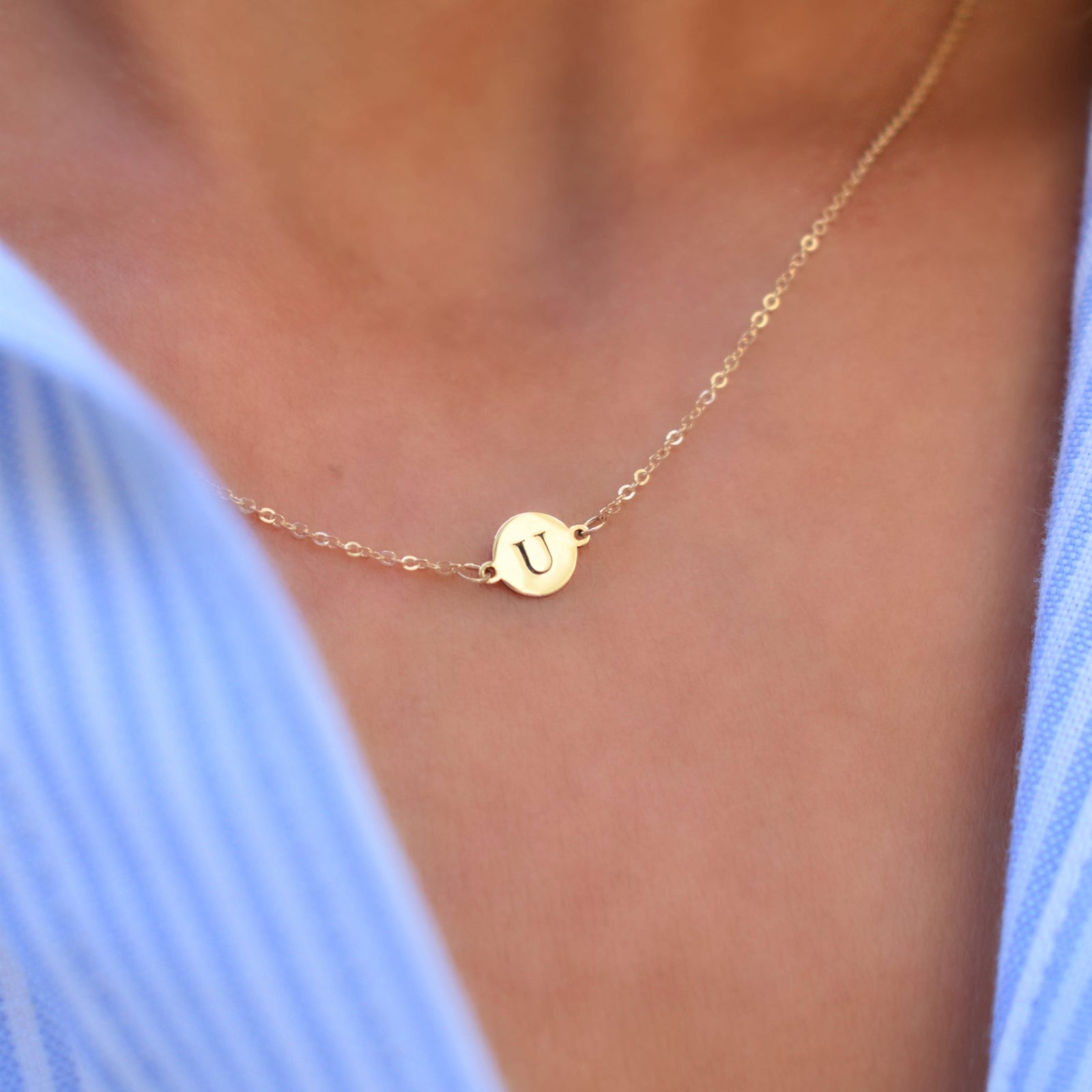 Woman with a 14k yellow gold cable chain necklace featuring one 1/4” flat disc engraved with the letter U