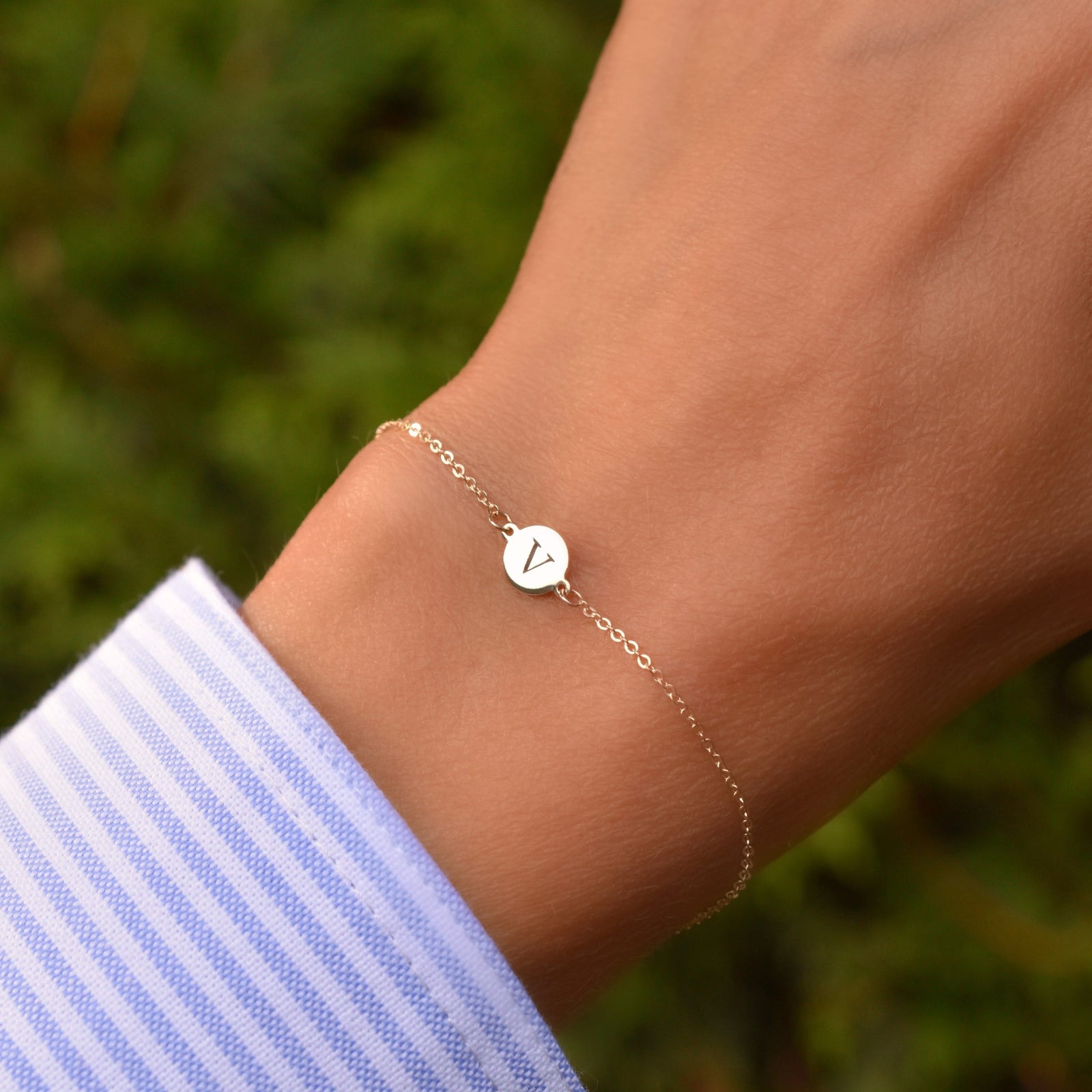 Woman wearing a 14k yellow gold cable chain bracelet featuring one 1/4” flat disc engraved with the letter V