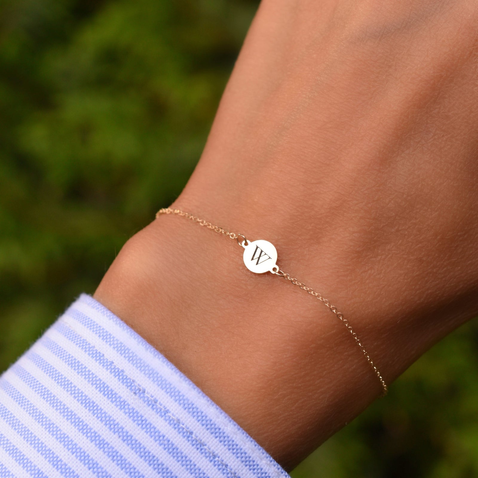 Woman wearing a 14k yellow gold cable chain bracelet featuring one 1/4” flat disc engraved with the letter W