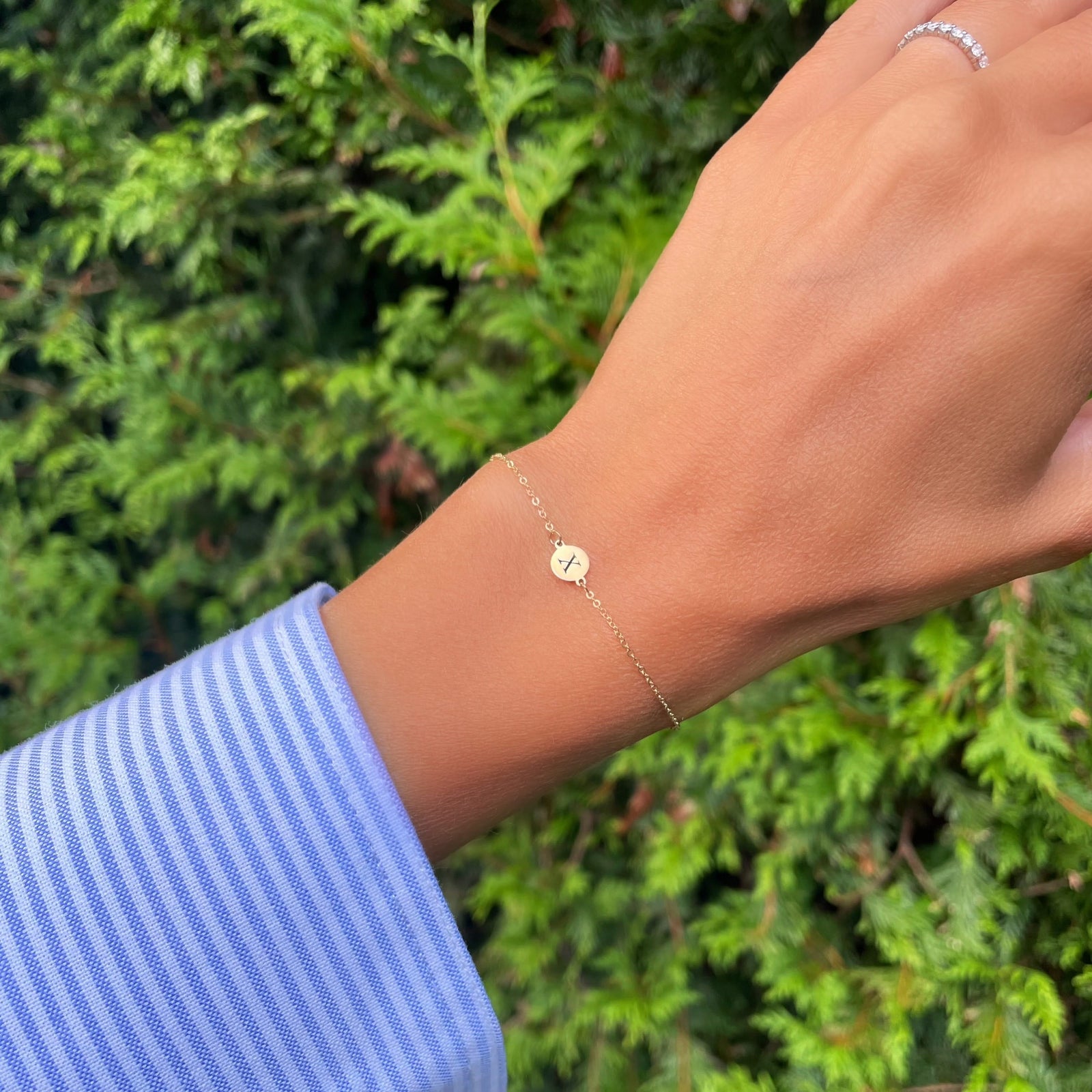 Woman wearing a 14k yellow gold cable chain bracelet featuring one 1/4” flat disc engraved with the letter X