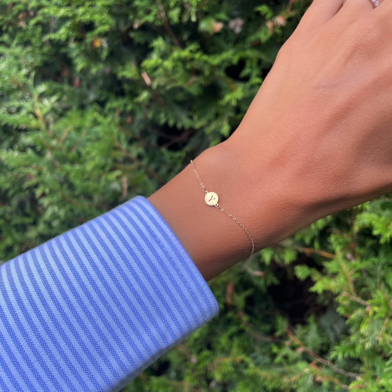 Woman wearing a 14k yellow gold cable chain bracelet featuring one 1/4” flat disc engraved with the letter Y
