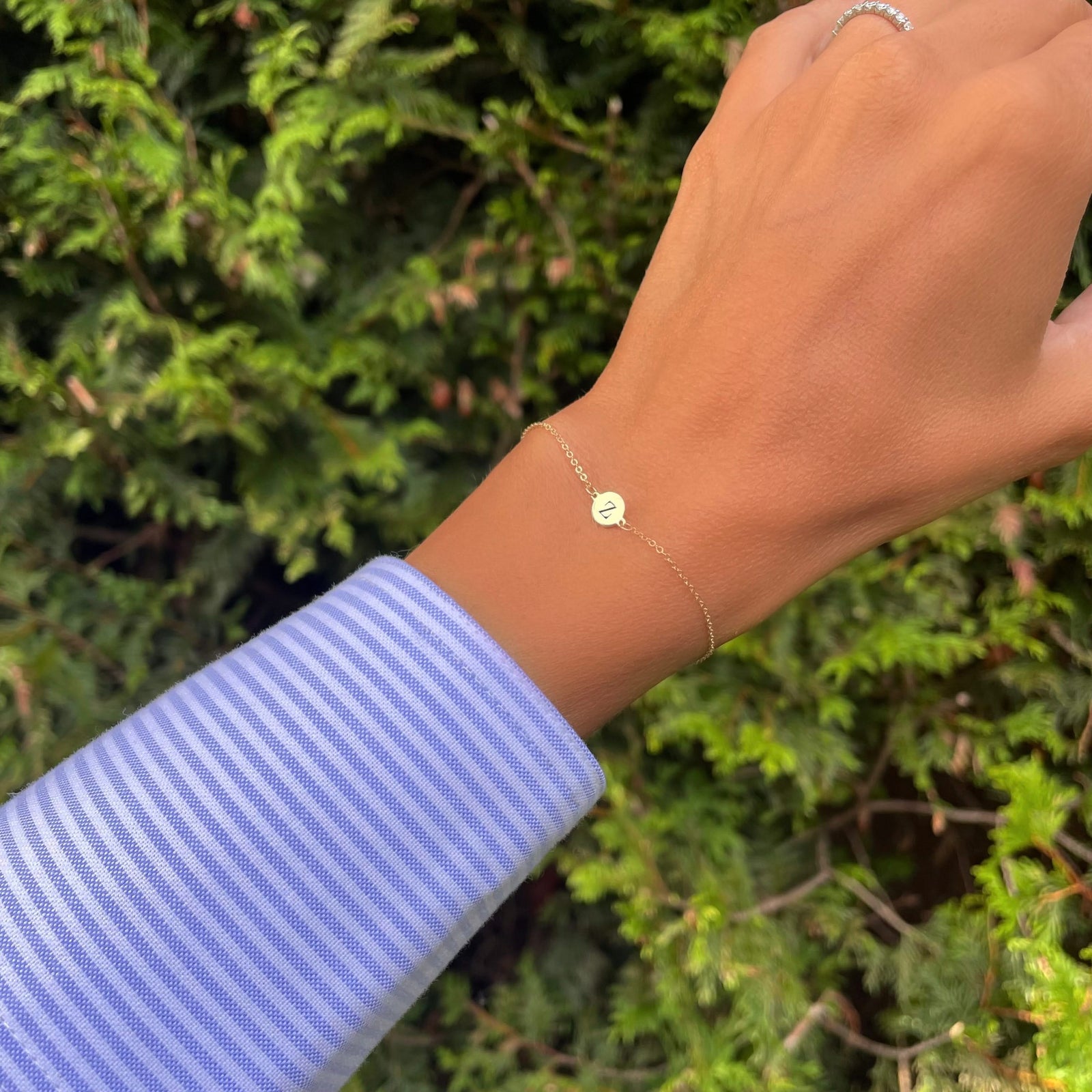 Woman wearing a 14k yellow gold cable chain bracelet featuring one 1/4” flat disc engraved with the letter Z