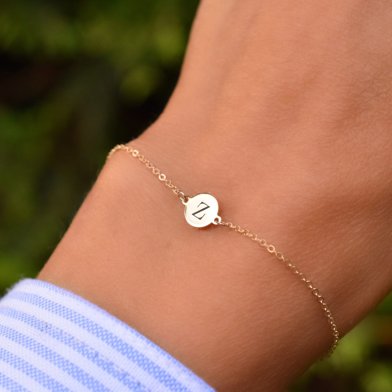Hand wearing a 14k yellow gold cable chain bracelet featuring one 1/4” flat disc engraved with the letter Z