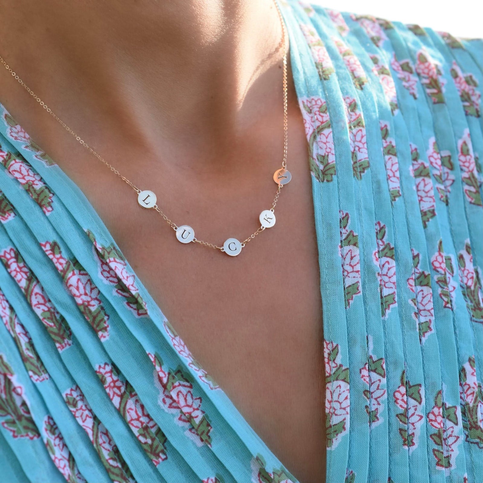 Woman wearing a 14k yellow gold cable chain necklace featuring five 1/4” flat engraved letter discs, spelling Lucky