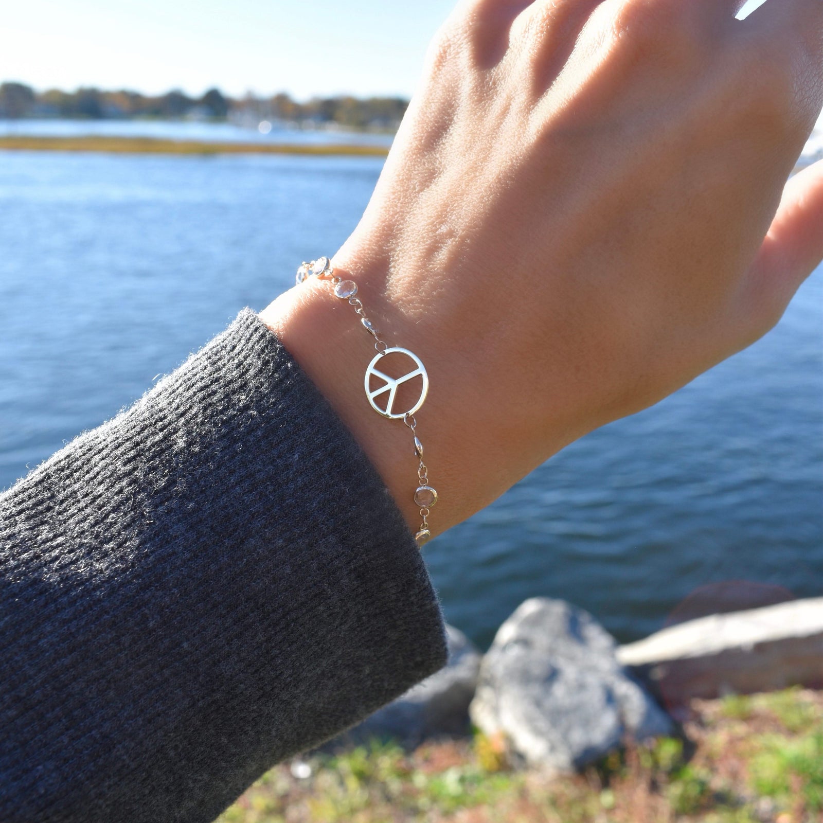 Woman with a Newport bracelet featuring one 1/2” cutout Peace Sign and 4 mm gemstones bezel set in 14k yellow gold