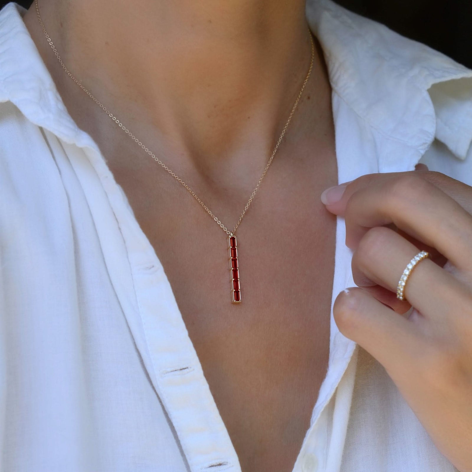 Woman wearing a Providence vertical bar pendant featuring 6 petite Garnet baguette stones set in 14k yellow gold