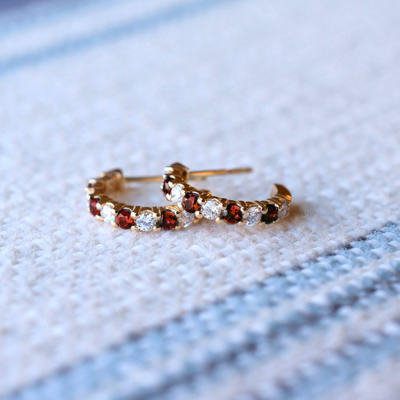 Pair of Rosecliff huggie earrings in 14k gold each featuring nine alternating 2 mm round cut garnets and diamonds
