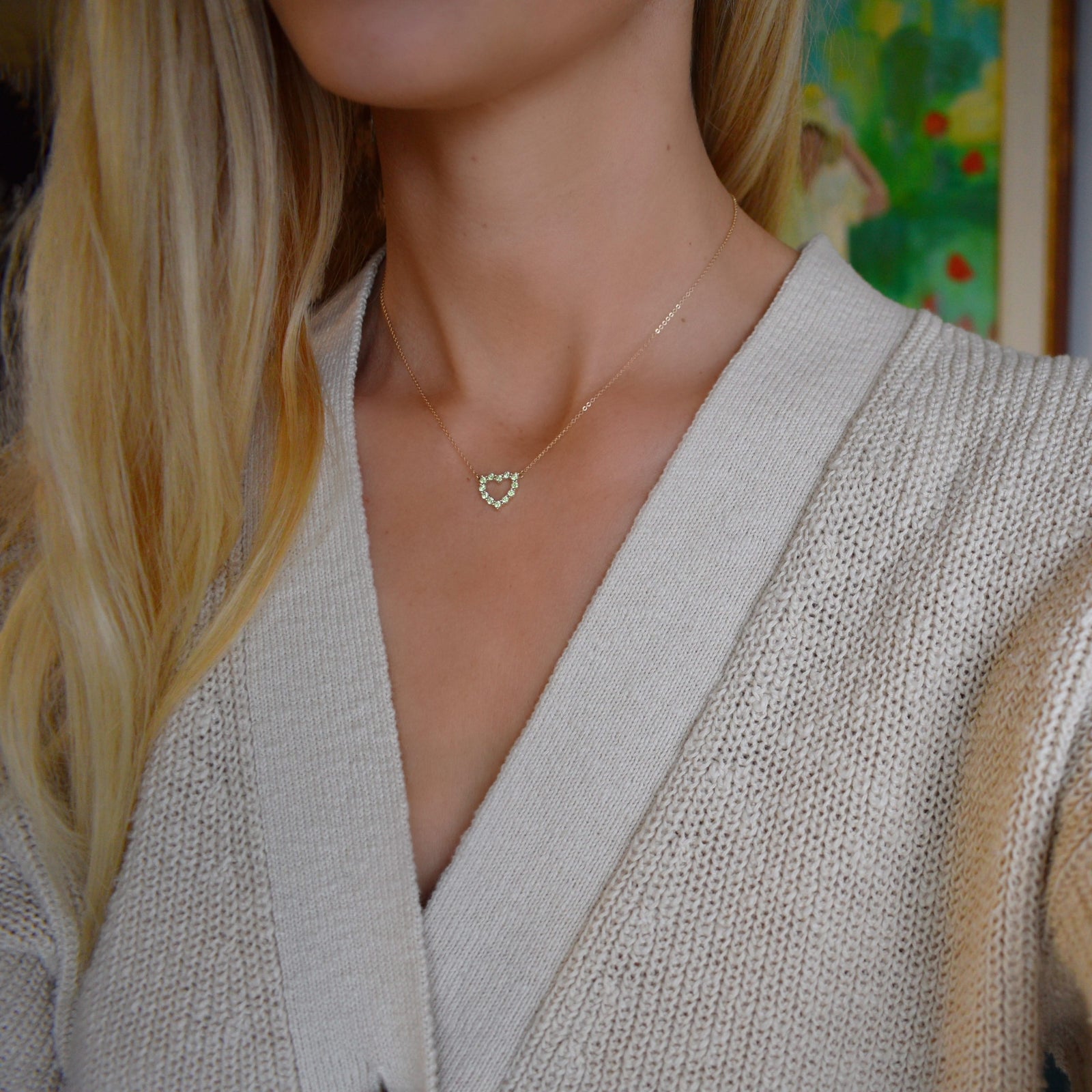 Woman with a Rosecliff Heart Necklace featuring twelve faceted round cut peridots prong set in 14k yellow Gold