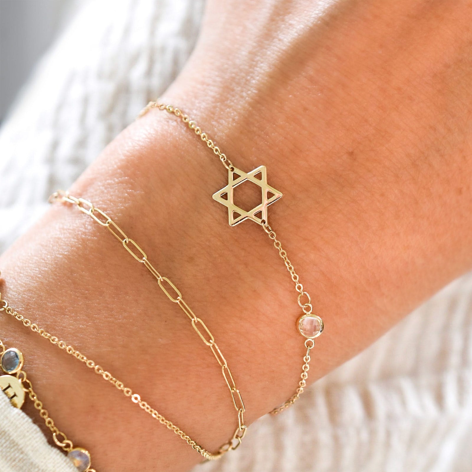 Woman wearinng multiple bracelets including a gold Classic bracelet featuring one birthstone and a 1/2" cutout Star of David