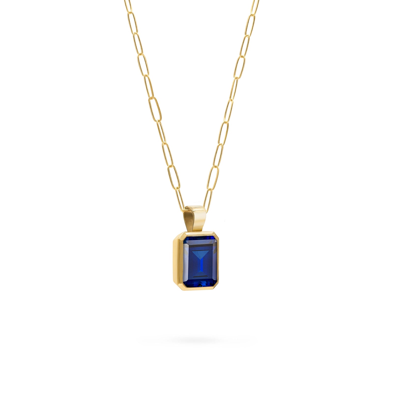 Adelaide paper clip chain and a Warren pendant with an emerald cut bezel set sapphire gemstone in 14k gold - angled view