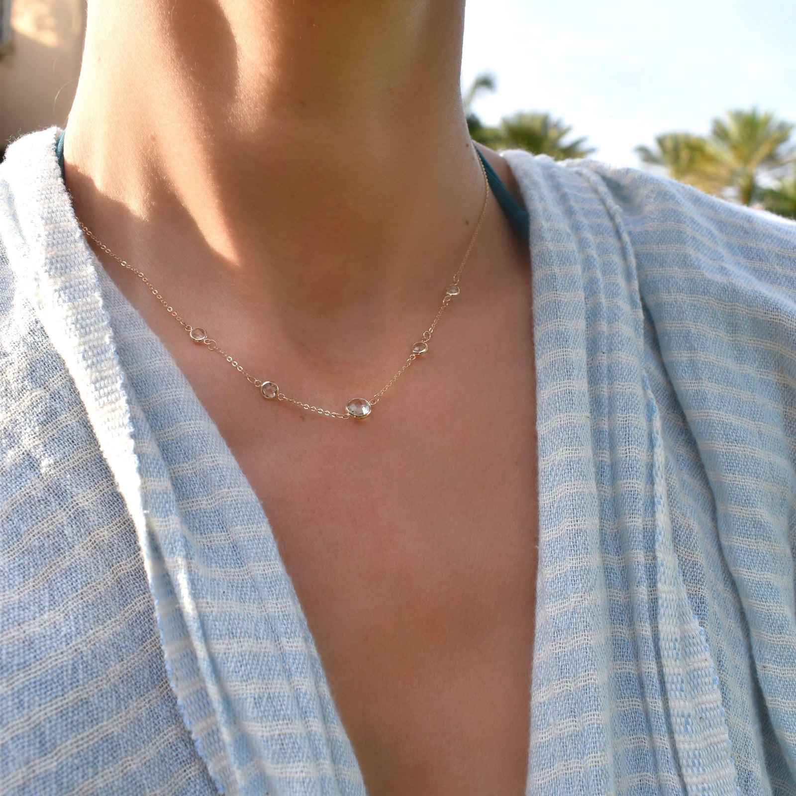 Woman wearing a Grand & Classic necklace featuring one 6 mm and four 4 mm White Topaz bezel set in 14k yellow gold