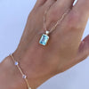 Braceleted woman's hand holding an Adelaide paper clip chain with a Warren Nantucket blue topaz pendant in 14k gold