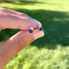 Woman holding a pair of 14k gold Greenwich 1 Birthstone earrings each featuring one 4 mm sapphire and one 2.1 mm diamond