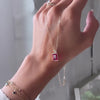 Braceleted woman's hand holding an Adelaide paper clip chain with a Warren emerald cut ruby pendant in 14k yellow gold