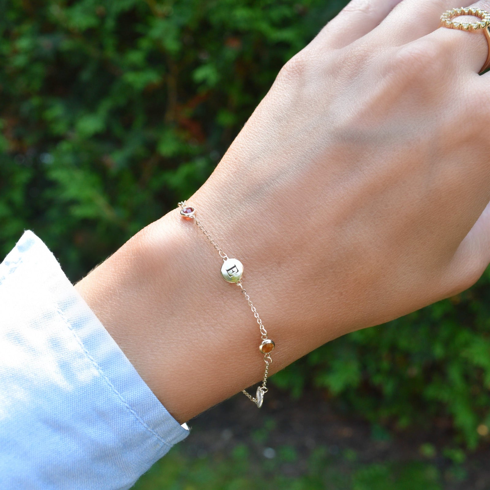 Woman wearing a 14k yellow gold Classic bracelet featuring birthstones and 1/4” flat letter-engraved discs