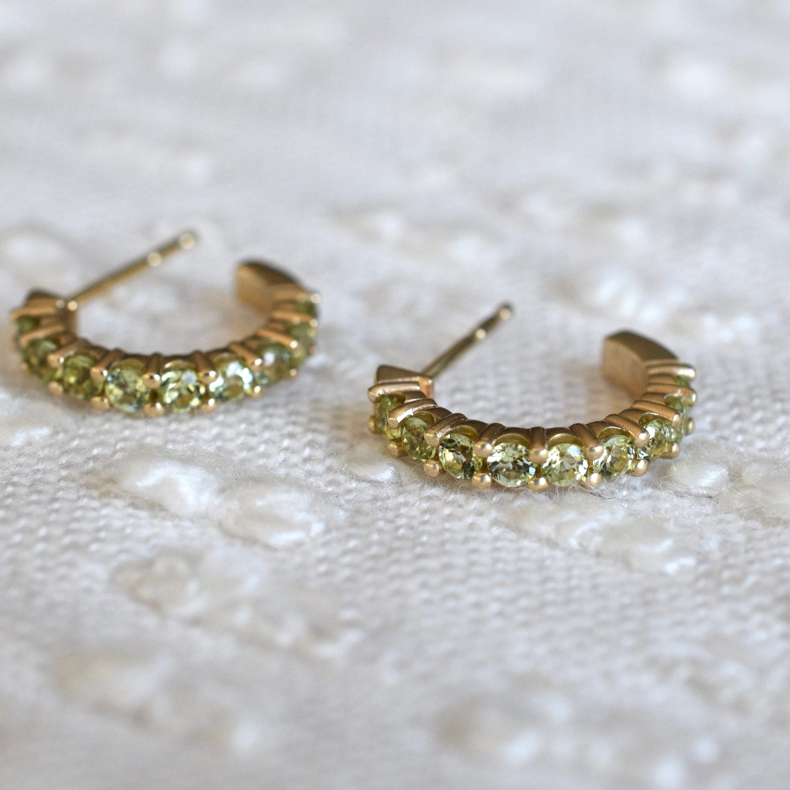 A pair of Rosecliff huggie earrings in 14k yellow gold each featuring nine 2mm faceted round cut prong set peridots