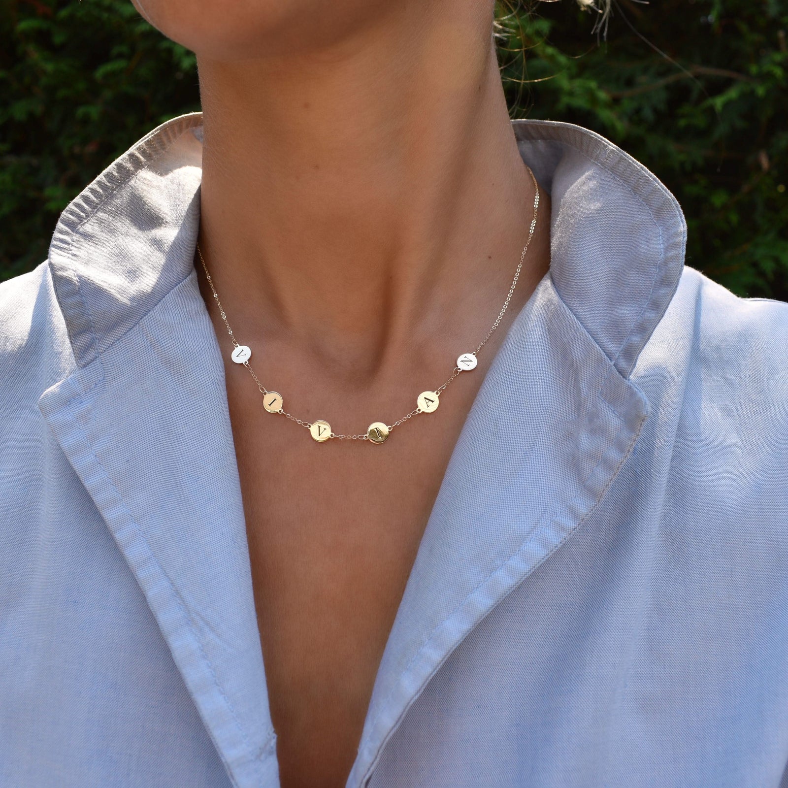 Woman with a 14k yellow gold cable chain necklace featuring six 1/4” flat discs engraved with letters