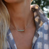 Woman wearing a Rosecliff bar necklace with eleven alternating 2 mm round cut emeralds and diamonds prong set in 14k gold