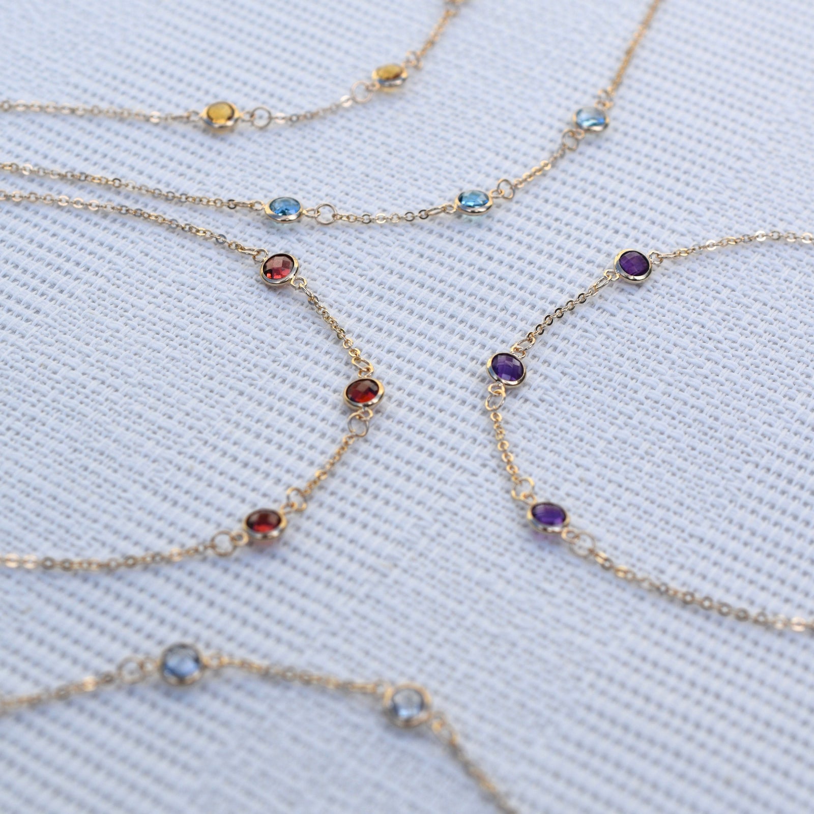 Multiple Bayberry 1.17 mm cable chain birthstone bracelets each featuring three 4 mm gemstones bezel set in 14k gold
