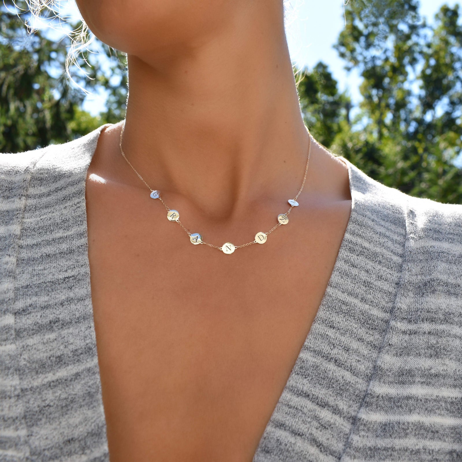 Woman wearing a 14k Yellow Gold cable chain Necklace featuring seven 1/4” flat engraved letter discs, spelling GRANDMA