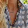 Woman wearing two necklaces including a Rosecliff bar necklace with 2 mm round cut sapphires prong set in 14k yellow gold