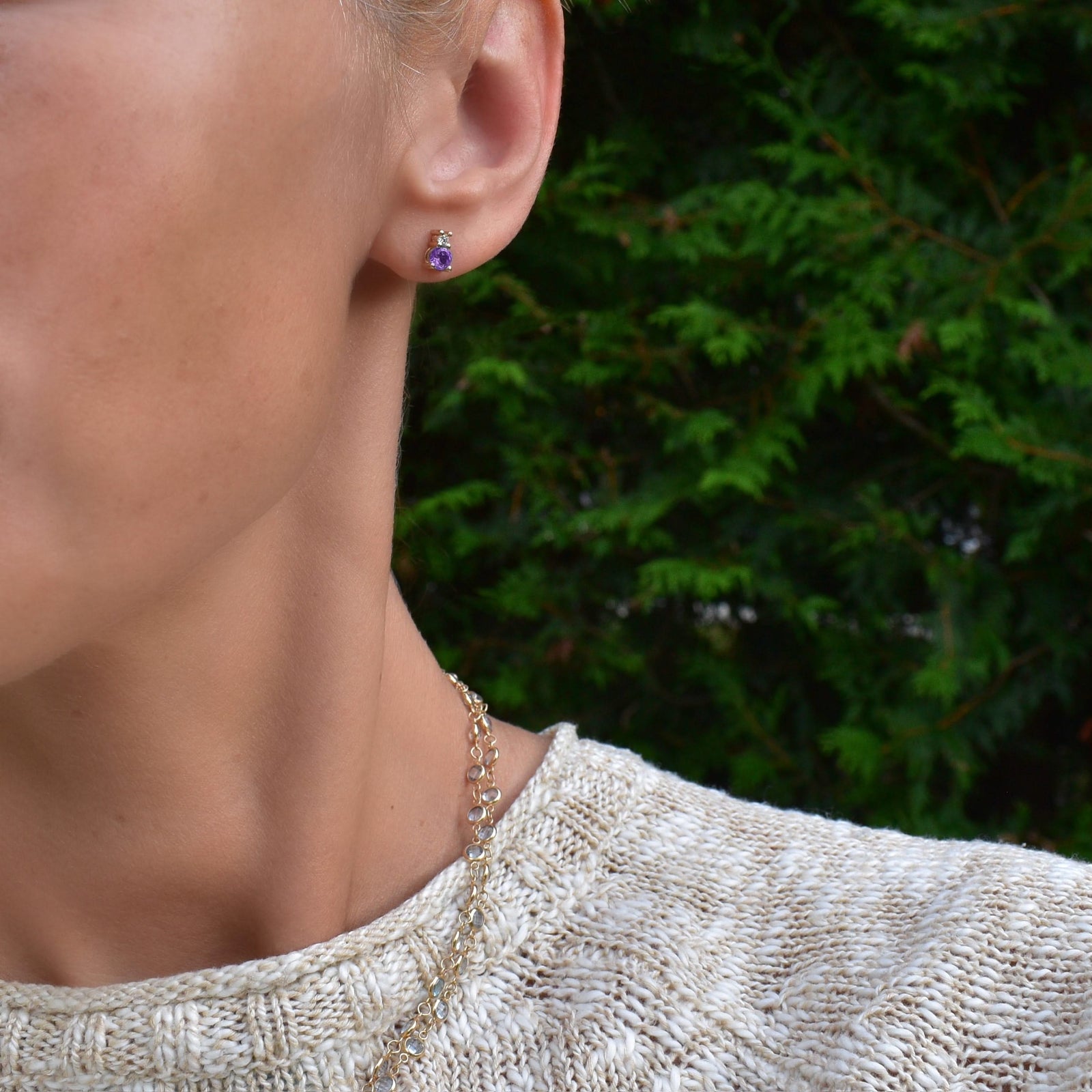 Woman wearing a 14k yellow gold Greenwich 1 Birthstone earring featuring one 4 mm amethyst and one 2.1 mm diamond