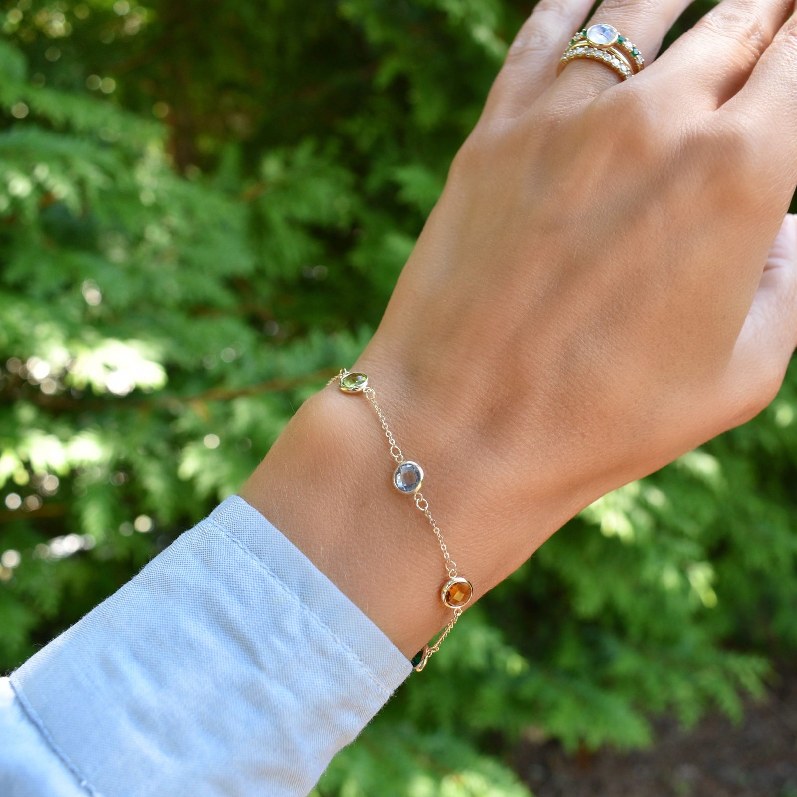 Woman wearing a Grand 1.17 mm cable chain bracelet in 14k gold featuring 6 mm briolette cut bezel set gemstones