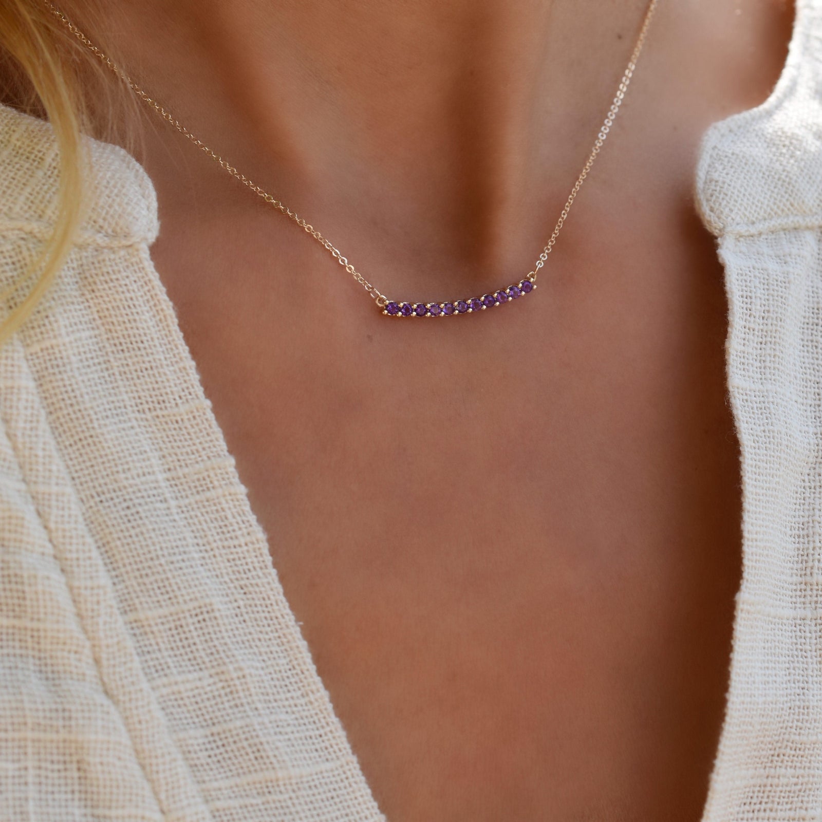 Woman wearing a Rosecliff bar necklace featuring eleven 2 mm faceted round cut amethysts prong set in 14k yellow gold