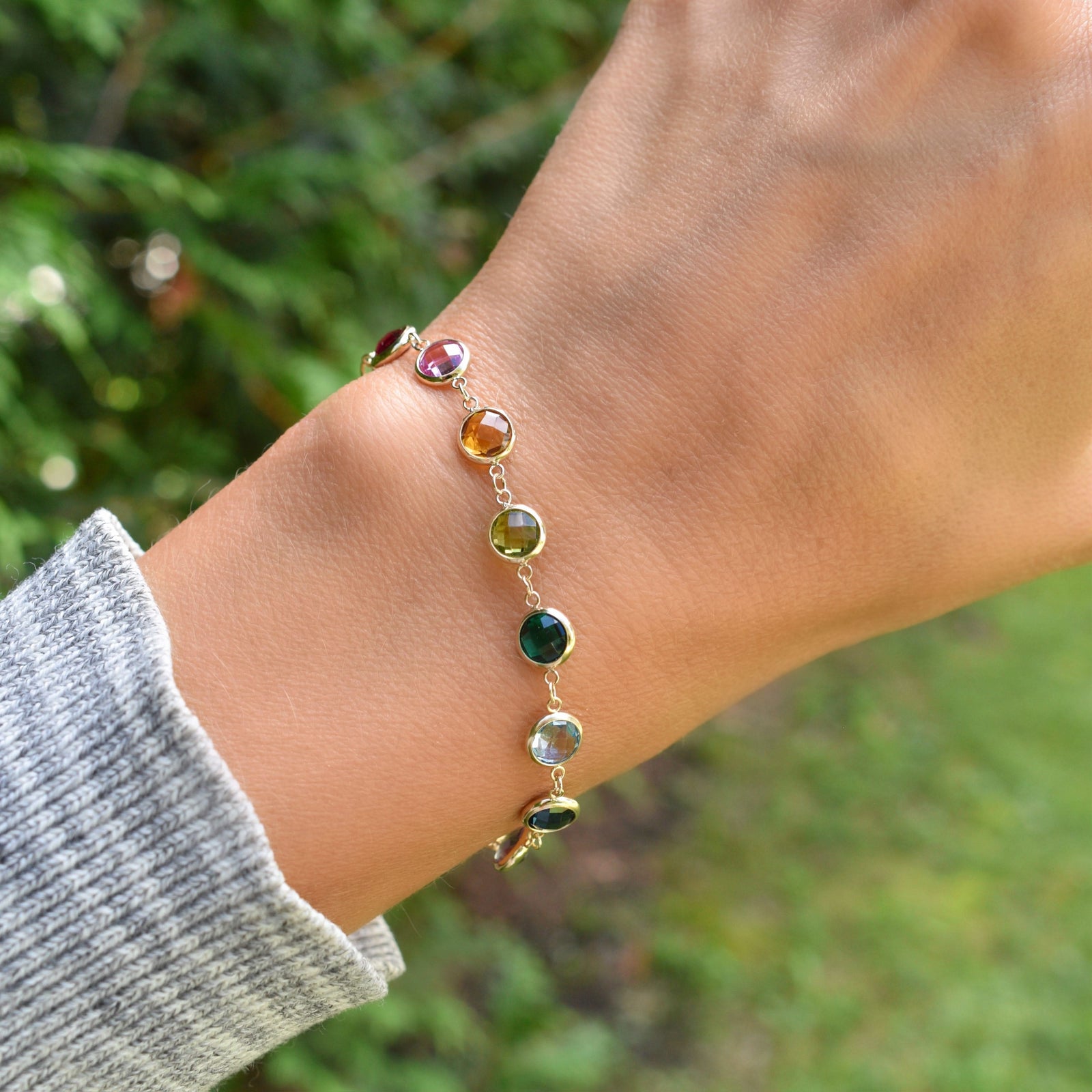 Woman wearing a Newport Grand 14k yellow gold bracelet featuring 6 mm rainbow hued briolette cut bezel set gemstones