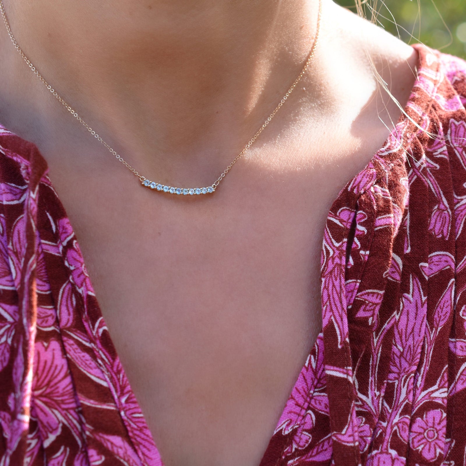Woman wearing a Rosecliff bar necklace featuring eleven 2 mm faceted round cut Nantucket blue topaz prong set in 14k gold