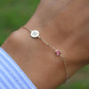 Woman wearing a 14k gold Classic bracelet featuring one pink tourmaline and one 1/4” flat disc engraved with the letter H