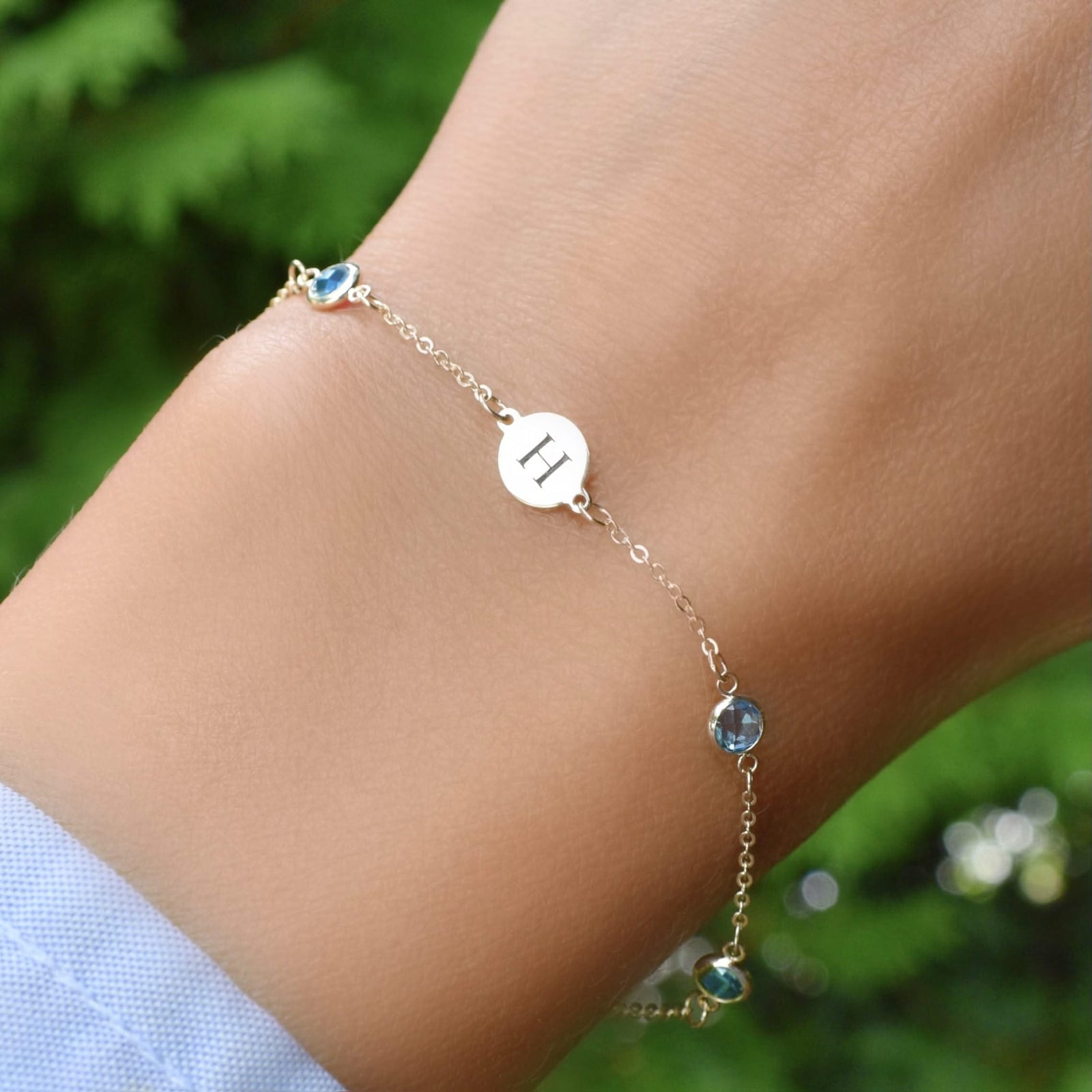 Woman wearing a 14k gold Classic bracelet featuring Nantucket blue topaz and one 1/4” flat disc engraved with the letter H