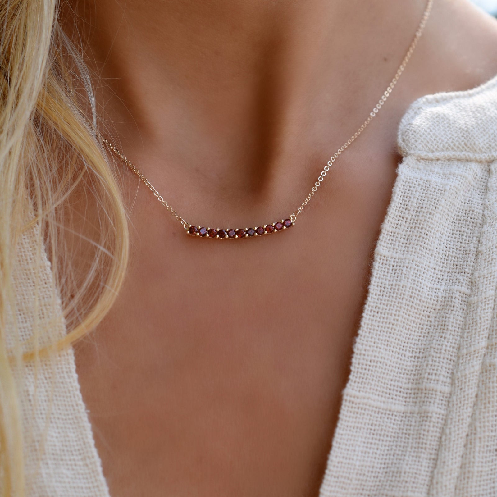 Woman wearing a Rosecliff bar necklace featuring eleven 2 mm faceted round cut garnets prong set in 14k yellow gold