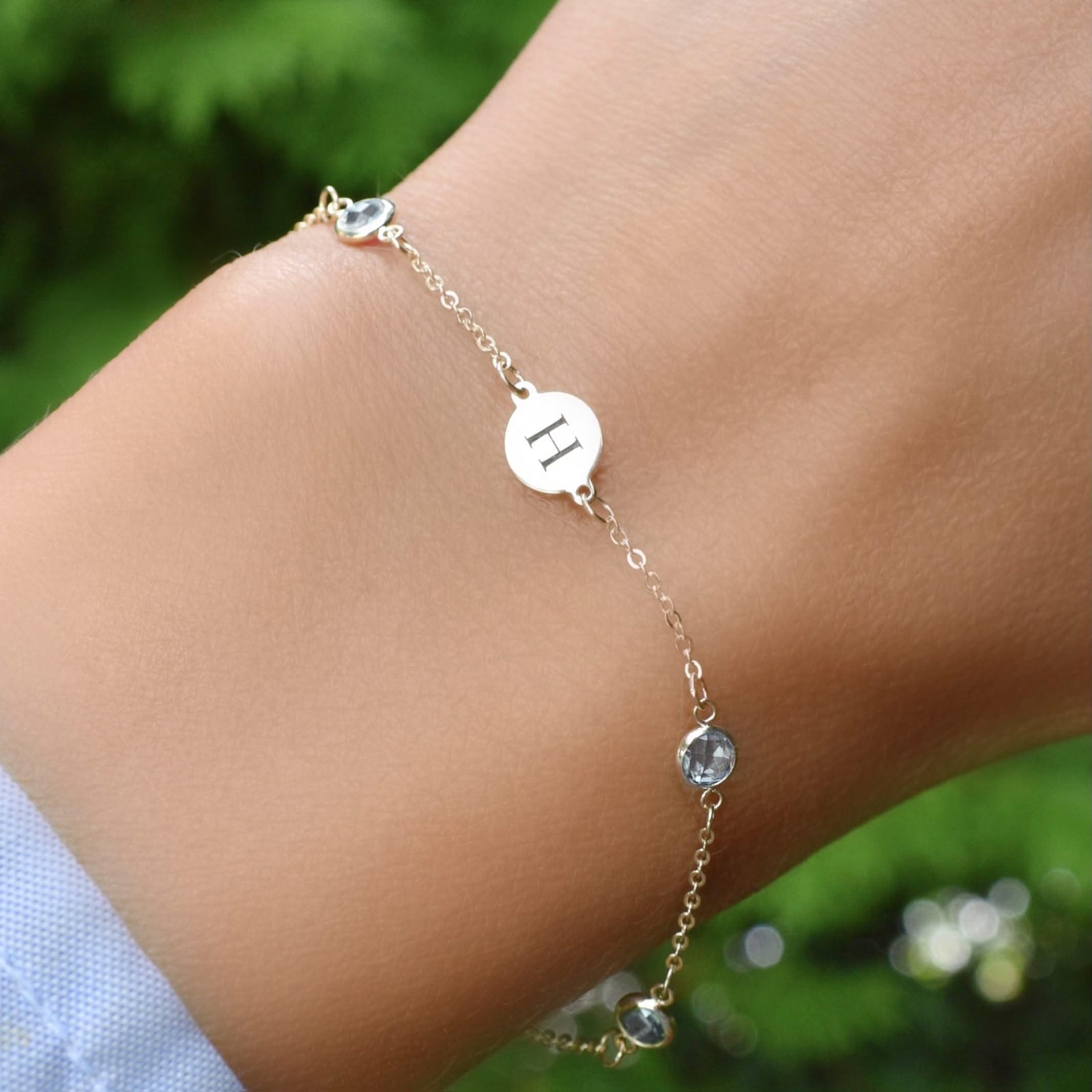 Woman wearing a 14k yellow gold Classic bracelet featuring aquamarines and one 1/4” flat disc engraved with the letter H