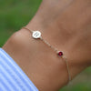 Woman wearing a 14k yellow gold Classic bracelet featuring one ruby and one 1/4” flat disc engraved with the letter H
